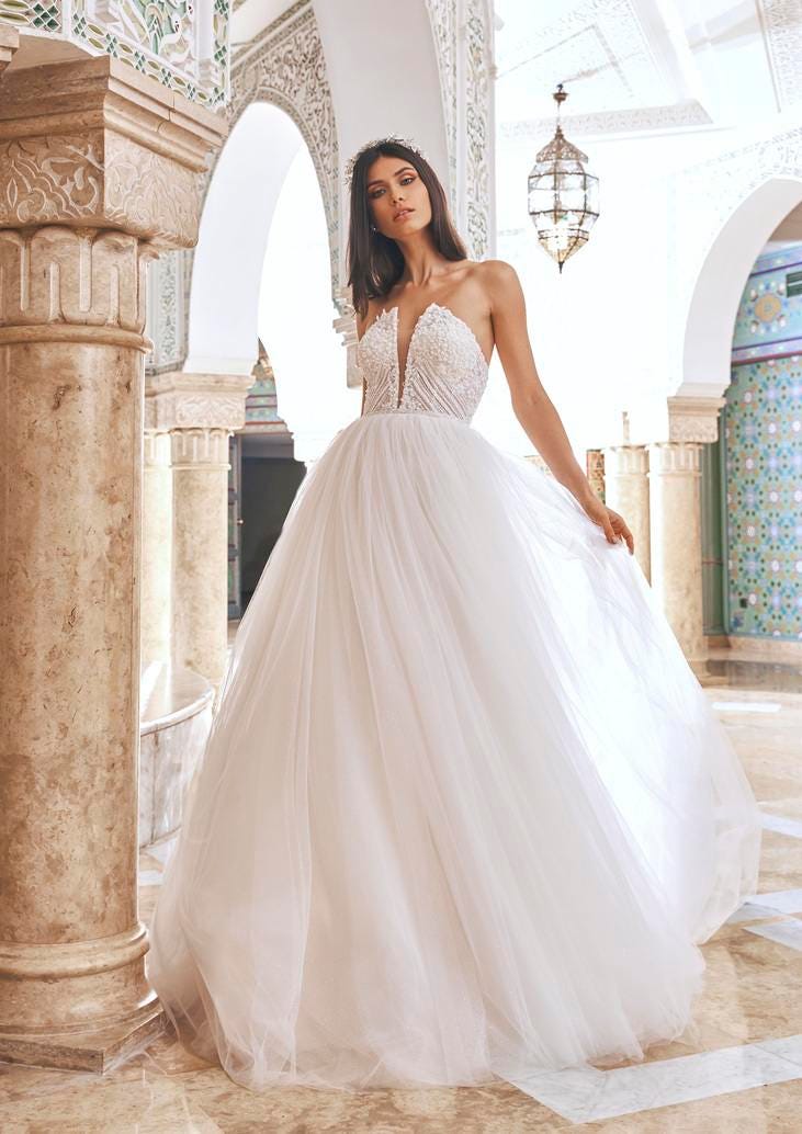 Une ravissante mariée dans une somptueuse robe de mariée bustier échancré se tient gracieusement dans un couloir.