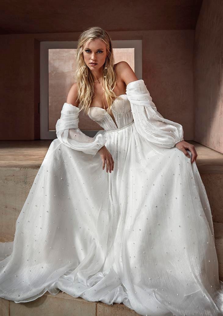 Mujer sentada con vestido de novia con mangas abullonadas de gasa y con los hombros al descubierto