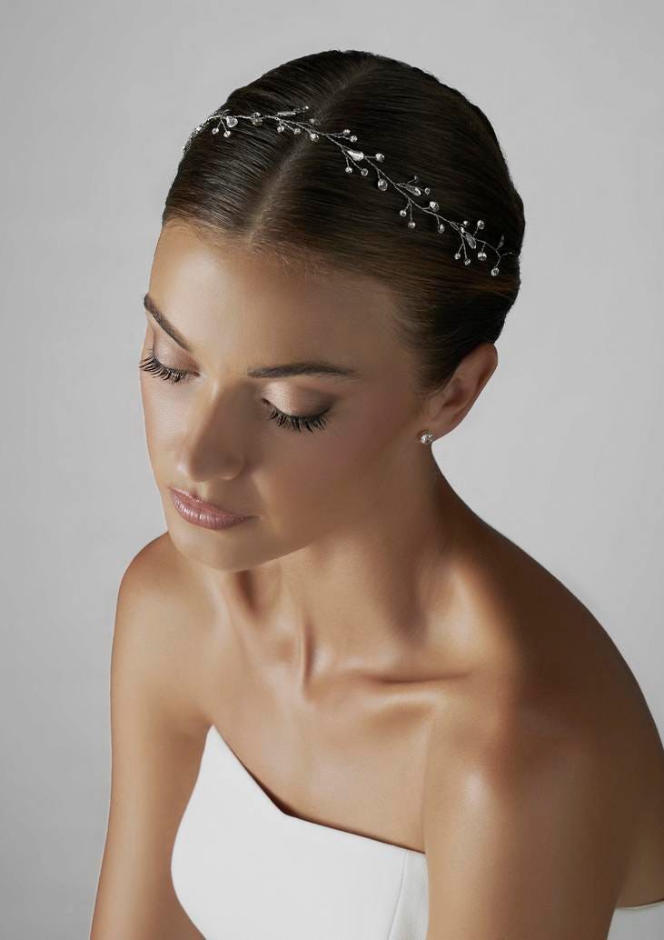 Brunette woman wearing a jeweled bridal headpiece with leaf detailing and strapless white wedding dress