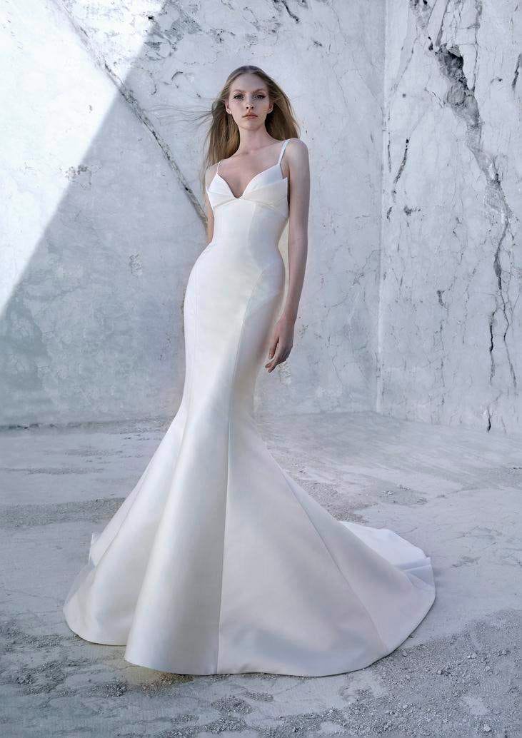 Mujer con un vestido de novia corte sirena de tirantes y el pelo suelto con paredes blancas detrás 