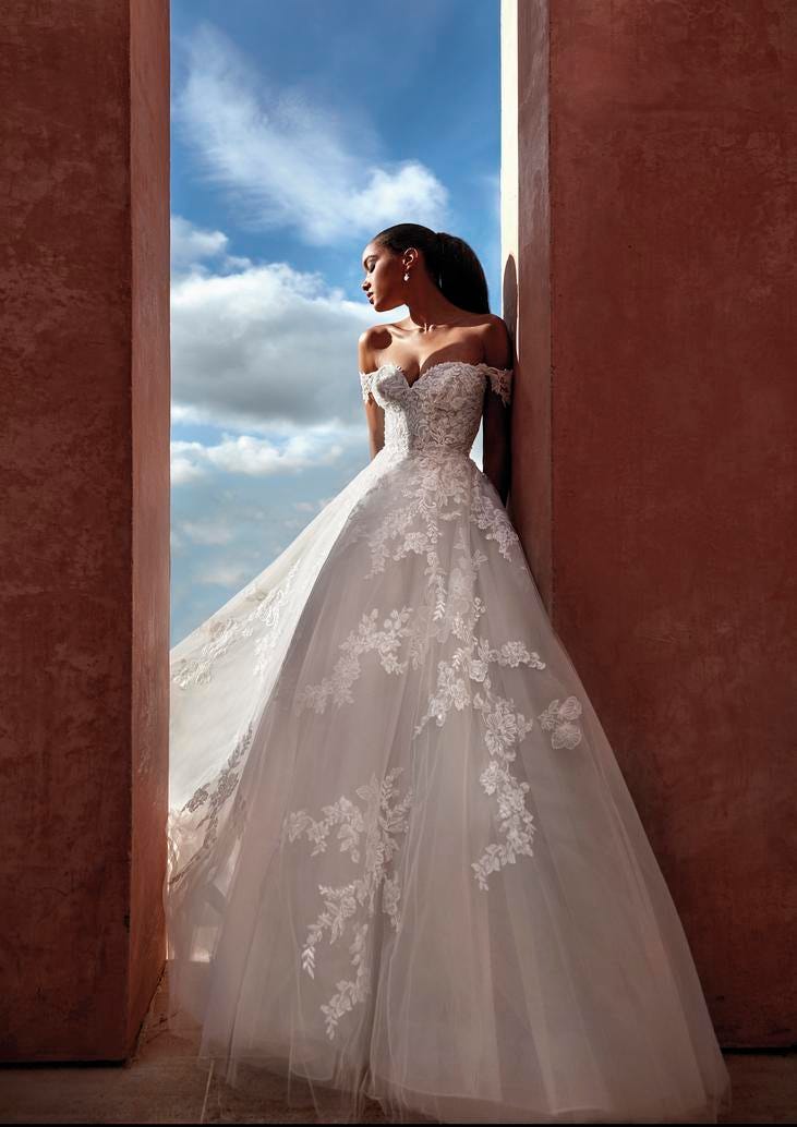 Femme en robe de mariée princesse romantique sans bretelles avec de la dentelle, qui s'appuie contre un mur.