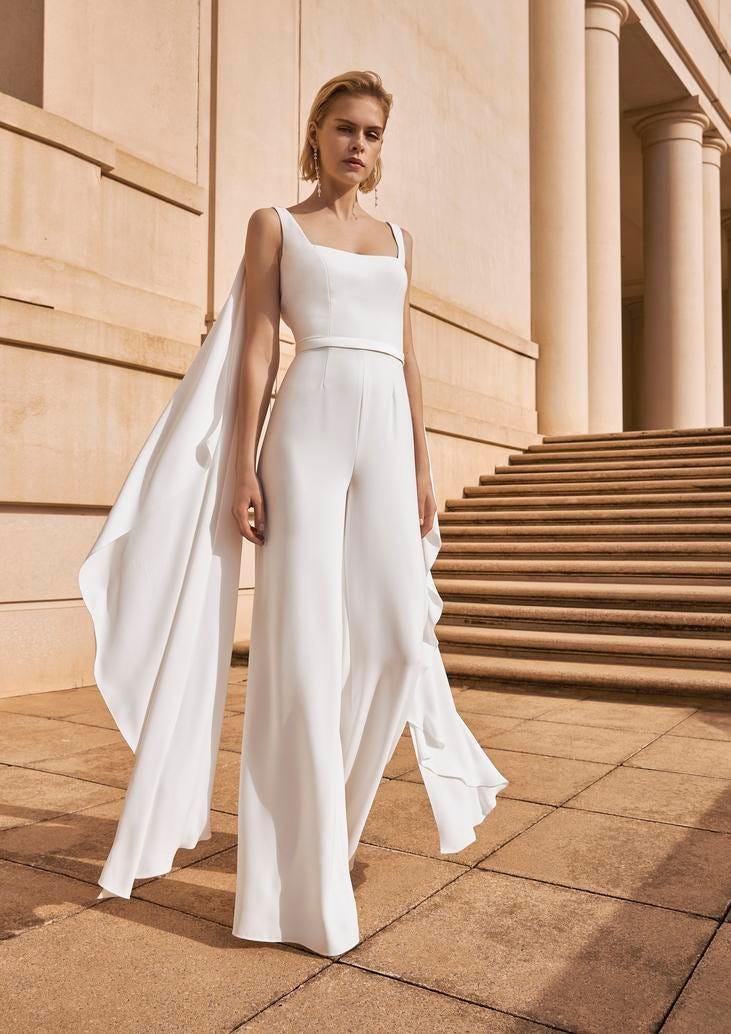 Une femme élégante en combinaison blanche et cape pour un mariage civil. Un look luxueux et sophistiqué.