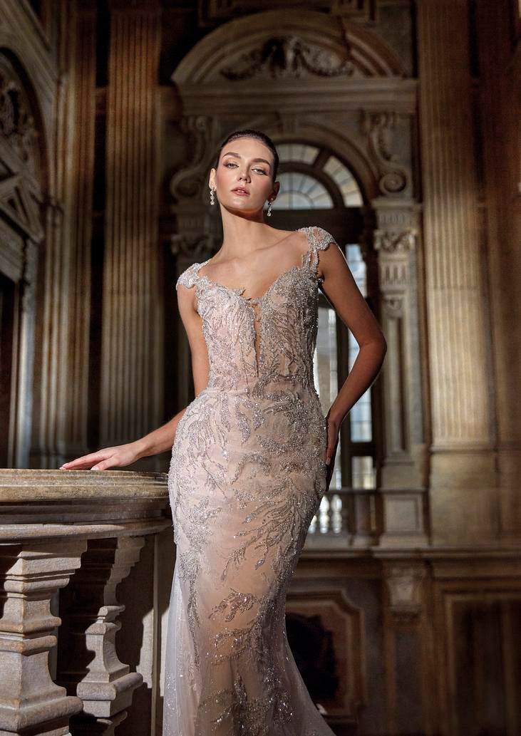 Brunette wearing a modern mermaid gown with a V-neck and metallic embroidery, posing on a marble staircase