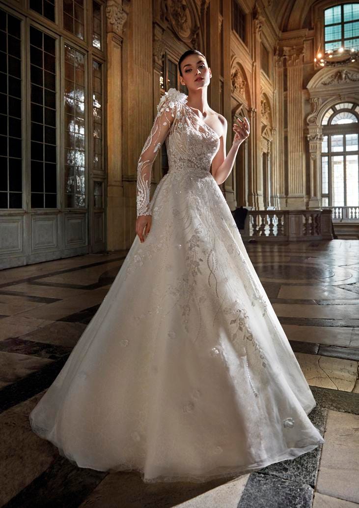Modella che indossa un lungo abito da sposa monospalla con manica lunga decorato