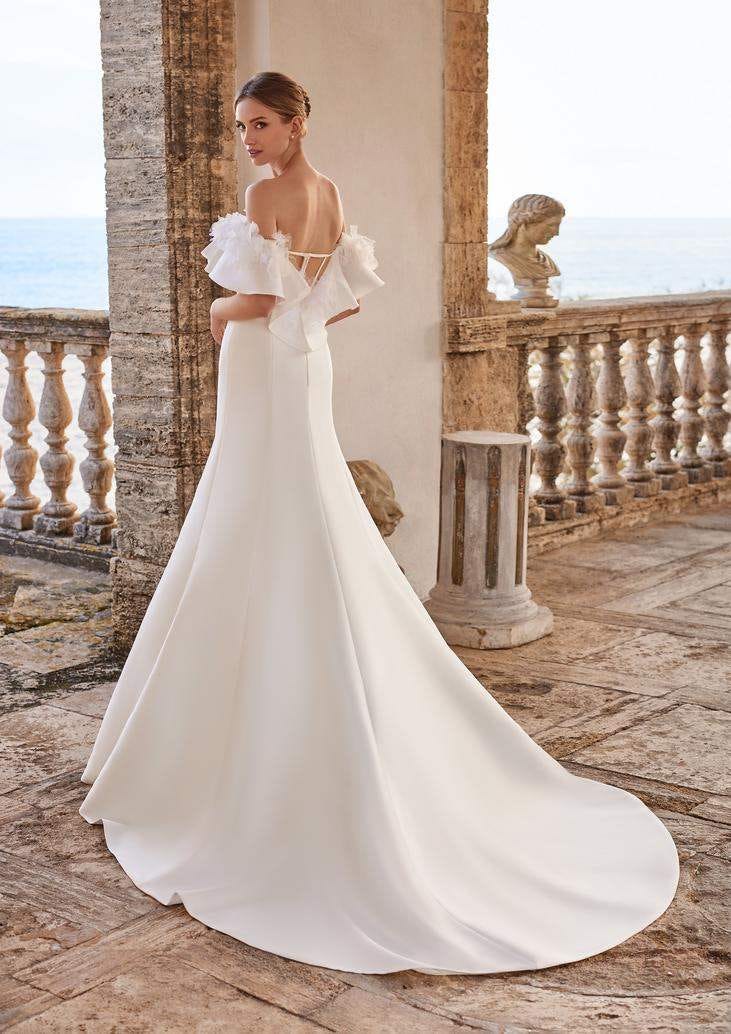 Modella di spalle che indossa un abito da sposa semplice ed elegante con strascico e scollatura sulla schiena.
