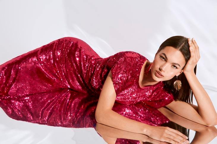 Mulher a posar deitada com um vestido de lantejoulas vermelho comprido coordenado com uns brincos