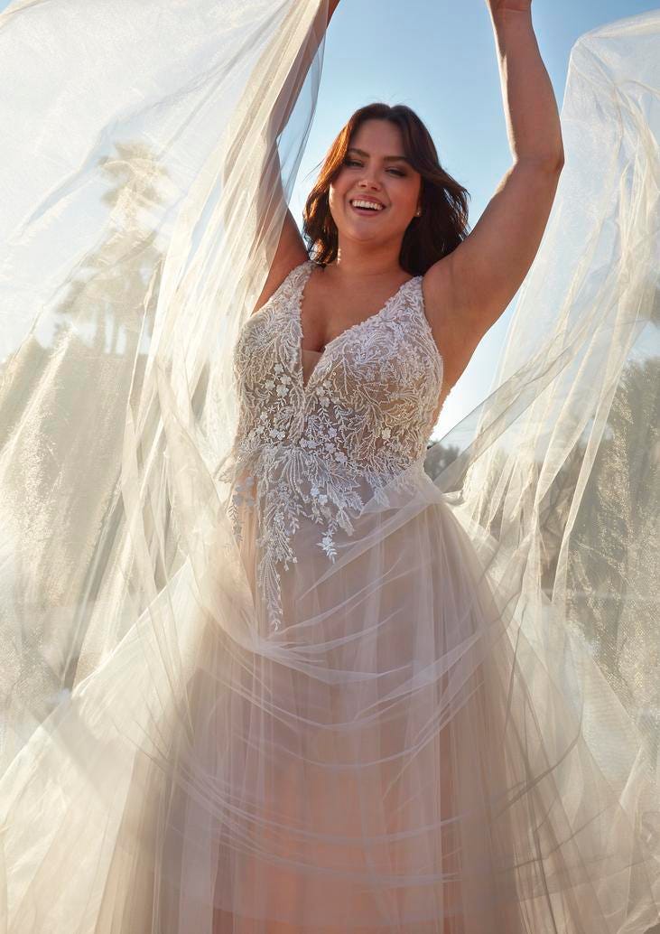 Mujer con vestido de novia plus size sujetando su velo riéndose con un vestido ampón de tul