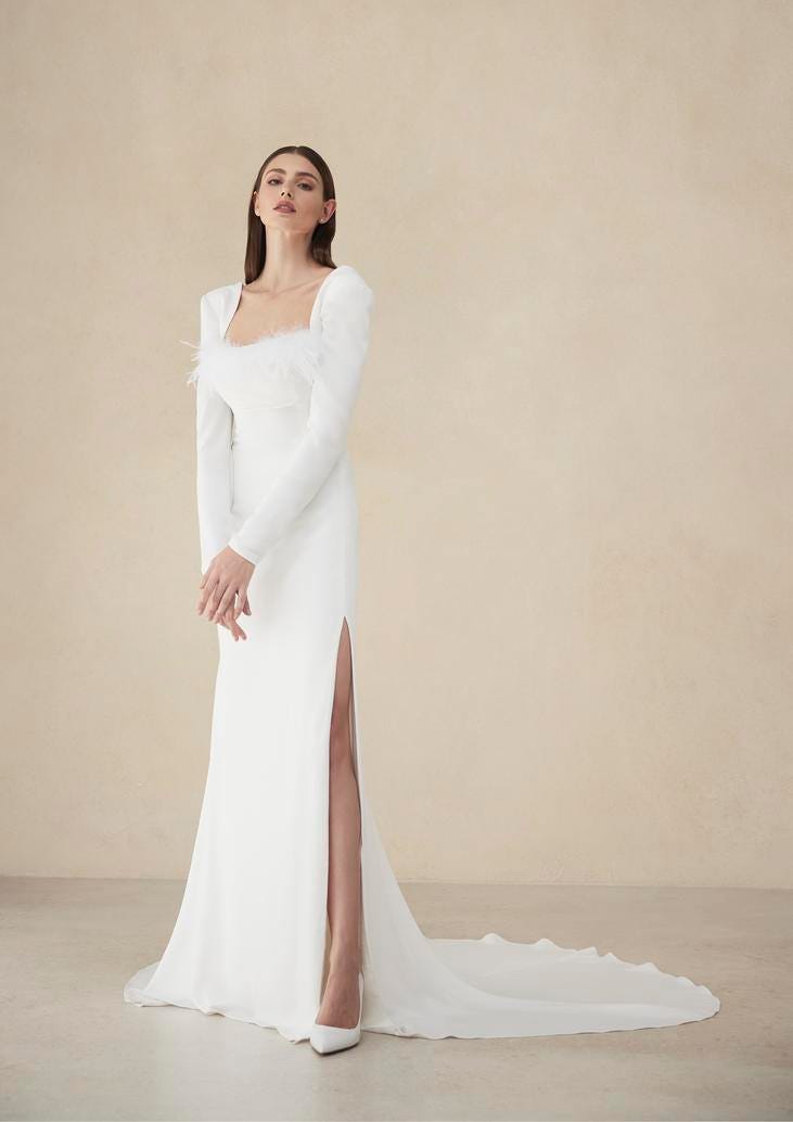 Modella che indossa un vestito da sposa elegante con maniche lunghe, scollo quadrato e scarpe décolleté bianche con tacco.