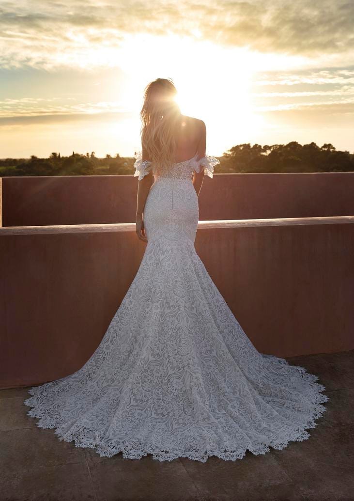 Frau mit weißem Brautkleid im Meerjungfraustil aus Spitze von hinten mit Sonnenuntergang