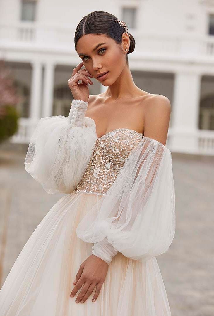 Une mariée ravissante dans une robe de mariée bustier perlée dotée de manches bouffantes amovibles et d'une jupe en tulle.