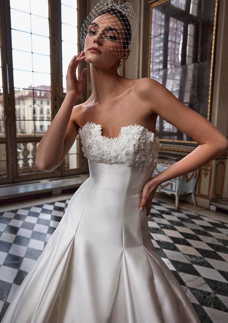 Modella che indossa un abito da sposa elegante senza spalline con decorazioni sul décolleté e manicure di colori neutri