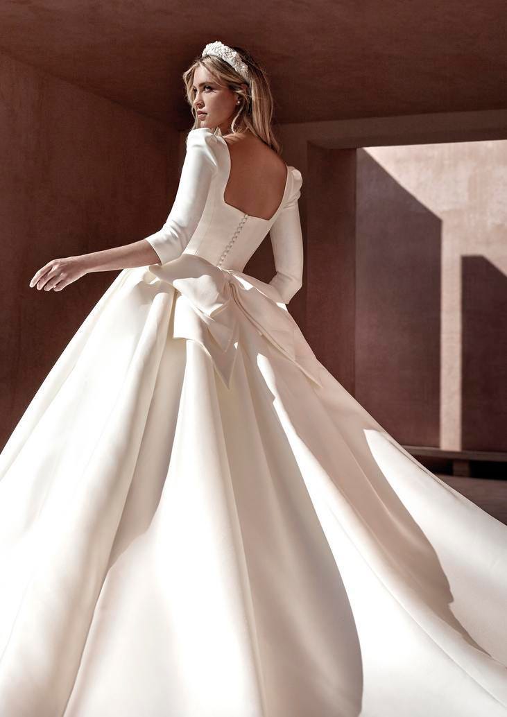 Noiva a posar de costas com um vestido de noiva princesa com um laço e botões conjugado com uma bandolete