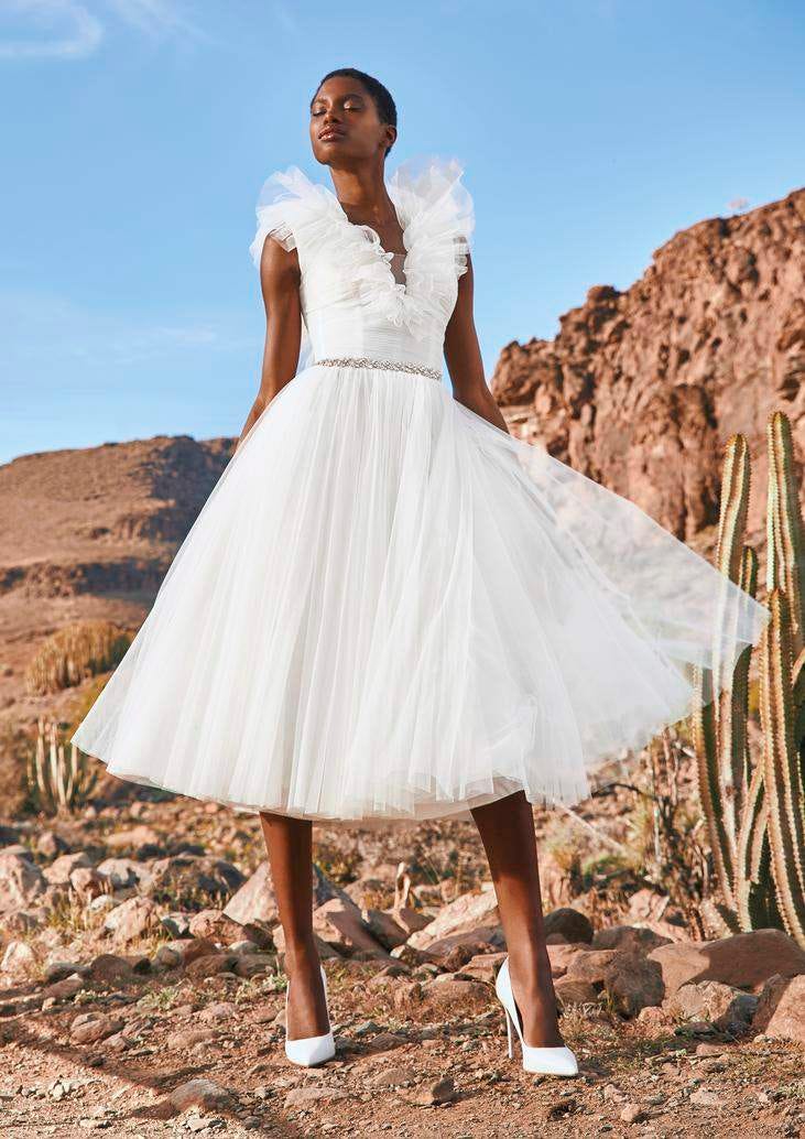 Noiva de cabelo curto a usar um vestido de tule curto conjugado com um cinto a sapatos fechados, numa paisagem desértica