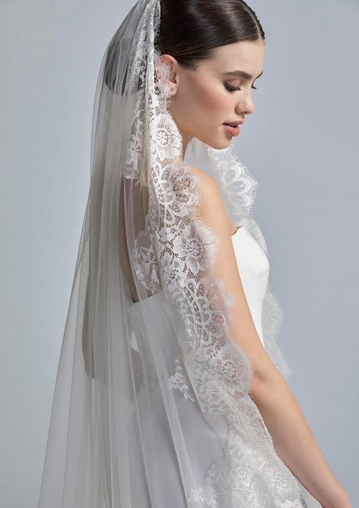 Noiva a usar um vestido liso branco com um longo véu de tule adornado com bordados
