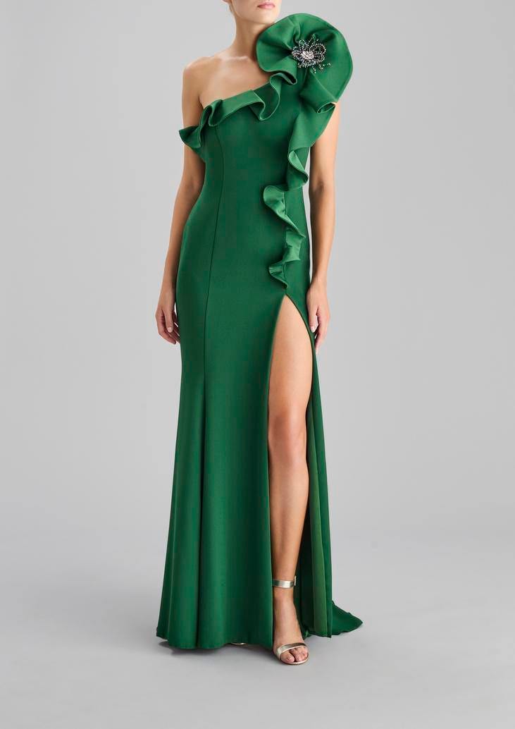 Convidada a usar um vestido longo verde de apenas uma alça elaborada com folhos, formando uma flor