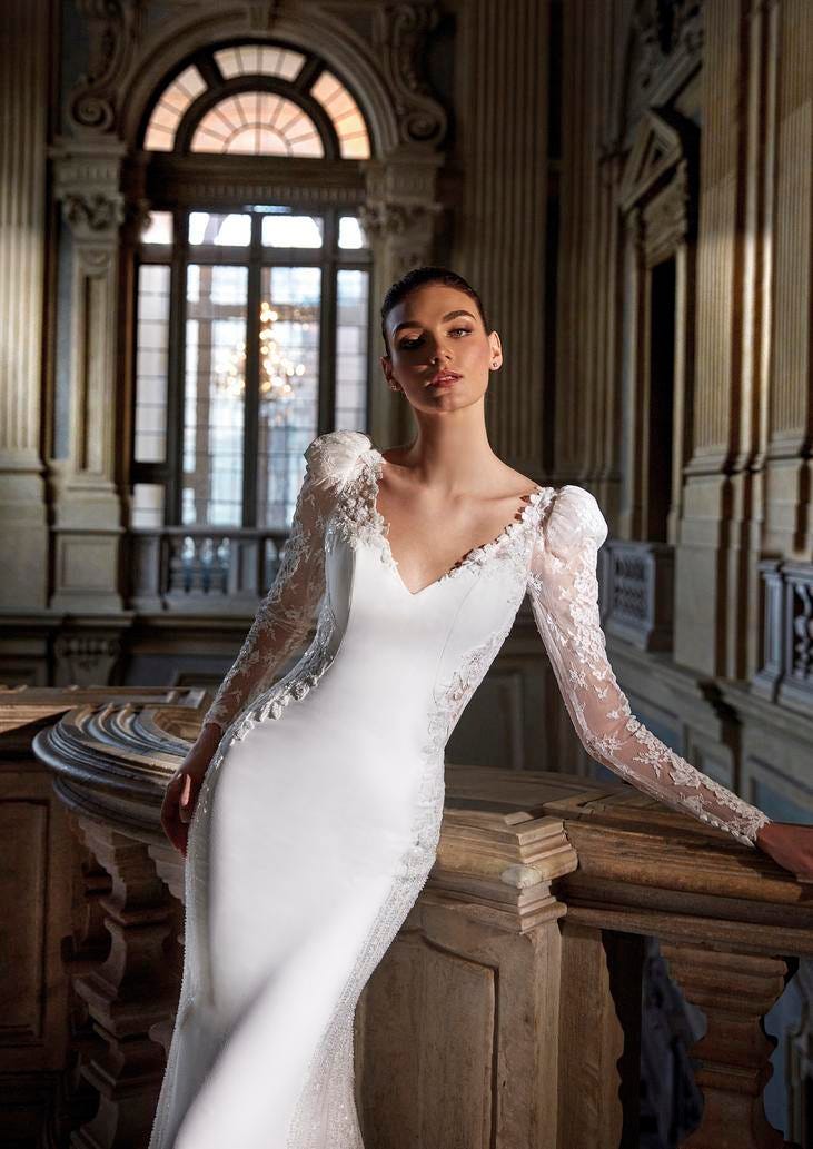 Woman wearing a mermaid crepe wedding dress with long lace sleeves, standing in a ballroom
