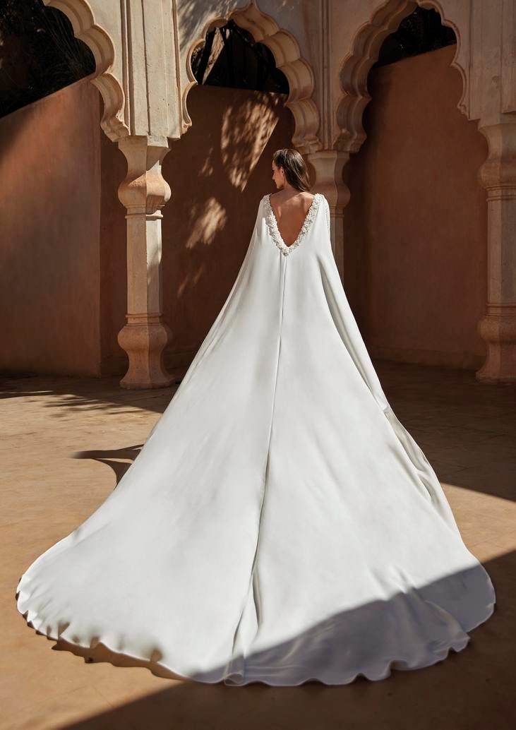 Woman wearing white bridal cape with deep V neck backline.