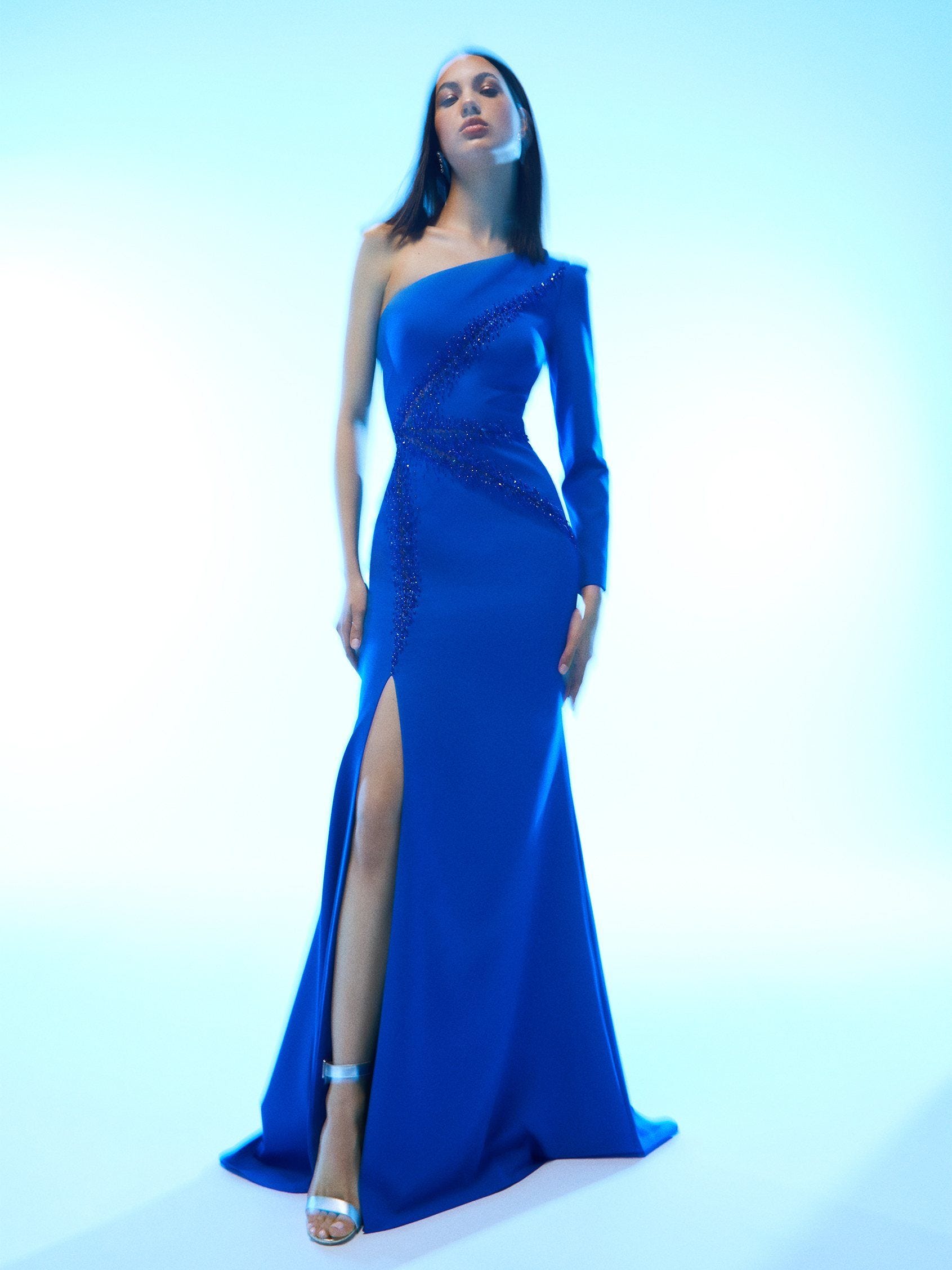 Mujer con vestido de invitada tendencia azul con escote asimétrico y abertura en la pierna.