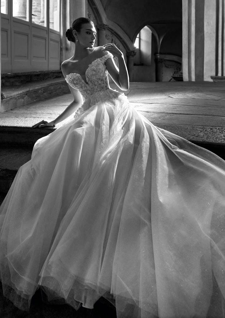 Frau in einem herzförmigen Brautkleid ohne Träger, hat ihr Hand auf der Schulter und schaut sie an, währrend sie auf einer Treppe sitzt. 