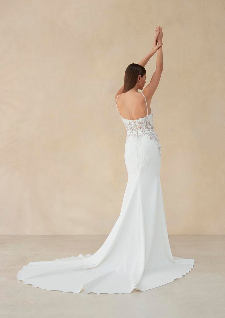 Brunette wearing a sleeveless wedding dress with low-back detail in crepe, holding her arms up
