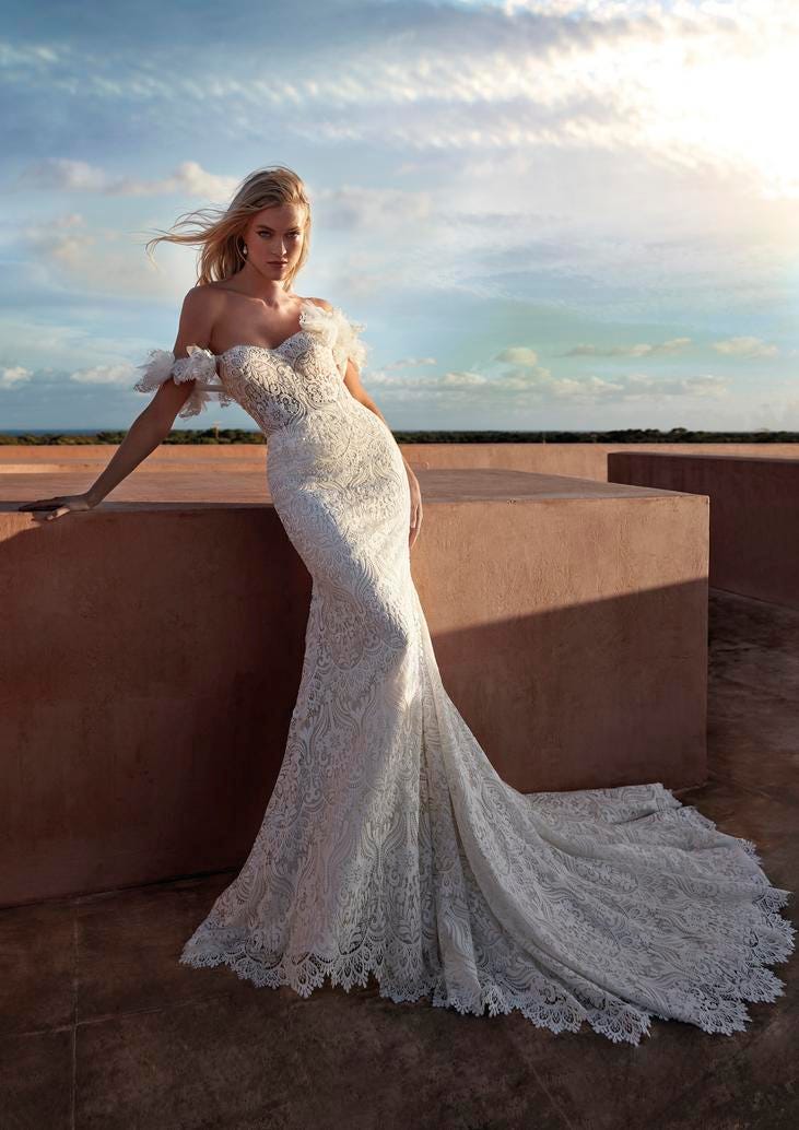 Blonde woman wearing a white lace mermaid wedding dress standing outside at sunset