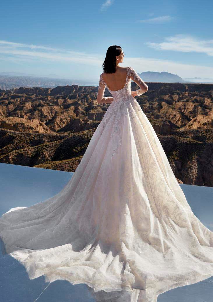 Frau mit braunen Haare im Hochzeitskleid steht von hinten draußen und schaut in die Ferne zu den Bergen.    