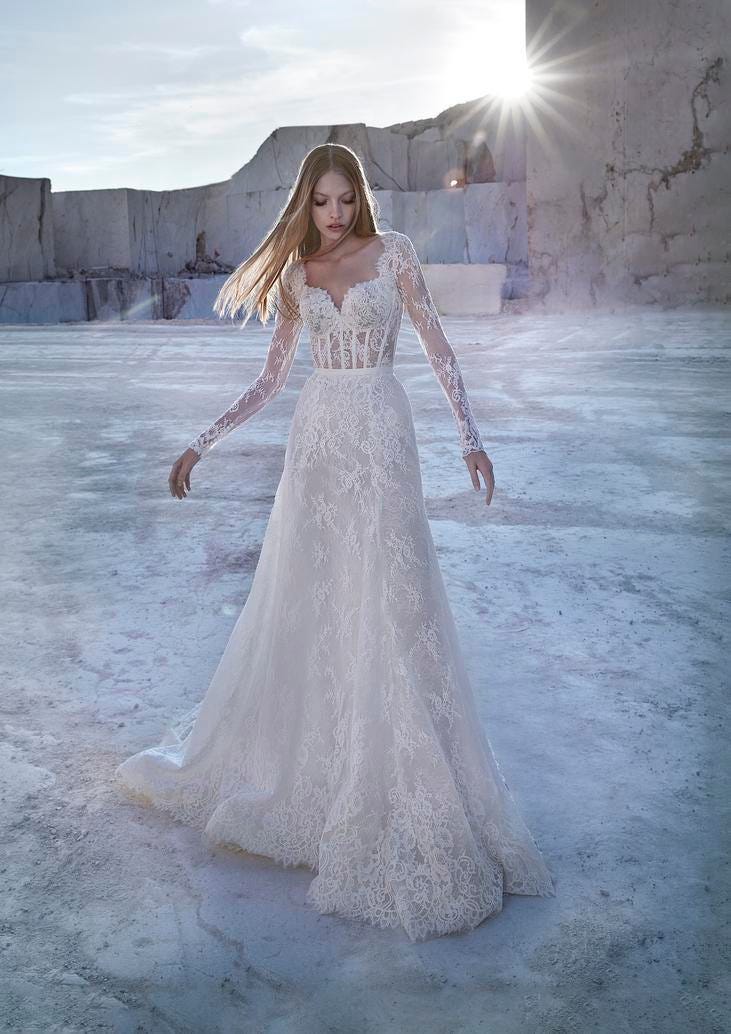 Blonde woman wearing a lace princess wedding gown with delicate long sleeves, standing outside