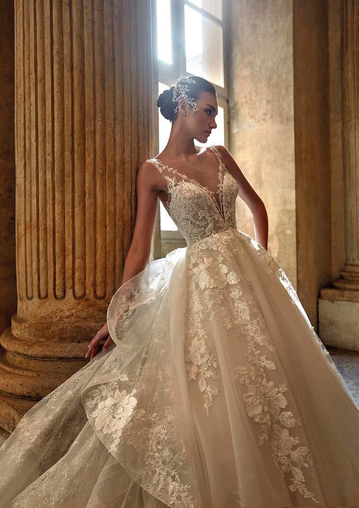 Brunette wearing a princess-cut glitter wedding gown with V-neck, leaning against a column in a ballroom 