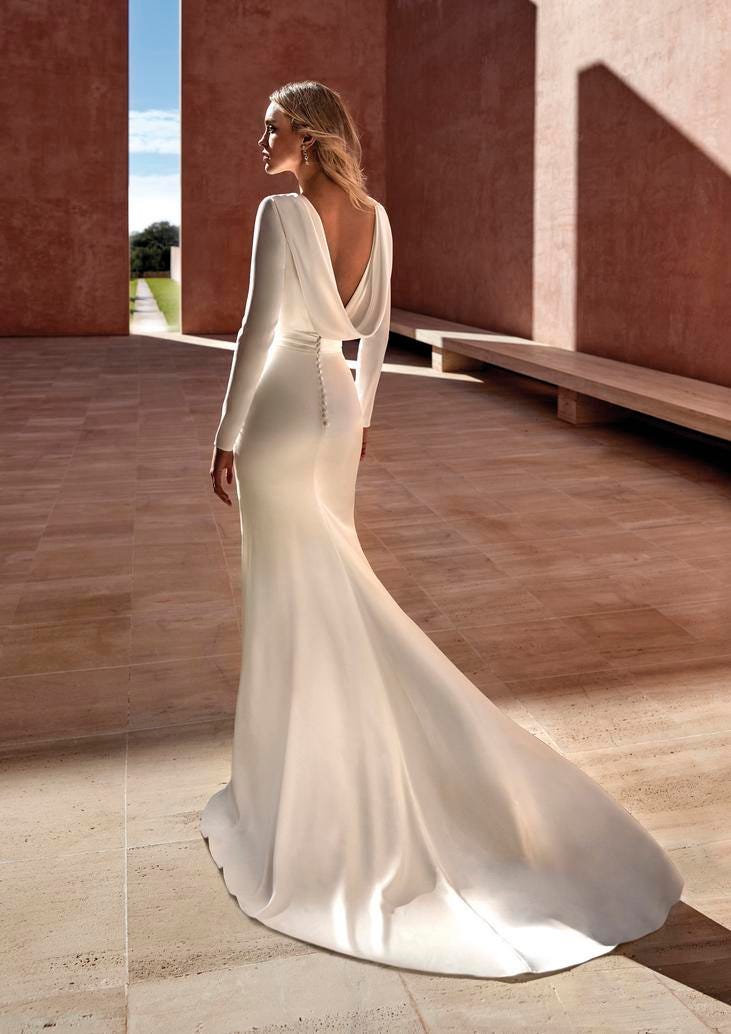 Blonde wearing a modern wedding with long sleeves and V-back detail, walking outside