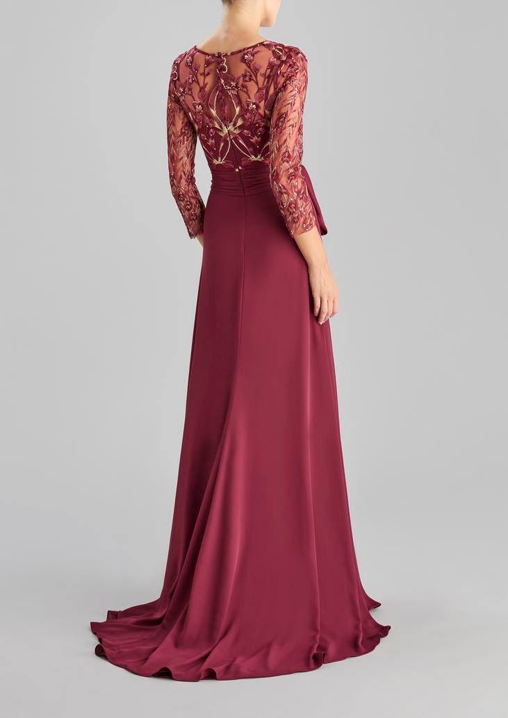 Woman wearing a long burgundy A-line party dress with three quarter sleeves and illusion neckline