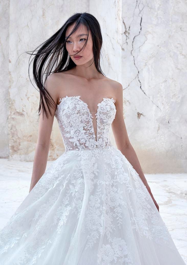 Brunette wearing a sleeveless princess wedding gown with a voluminous lace-trimmed skirt, standing outside