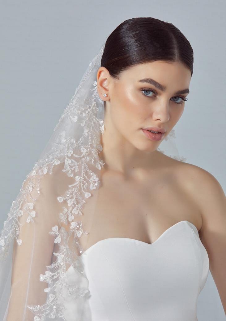 Brunette wearing a strapless wedding gown and an off-white bridal veil with delicate beadwork, featuring a floral motif