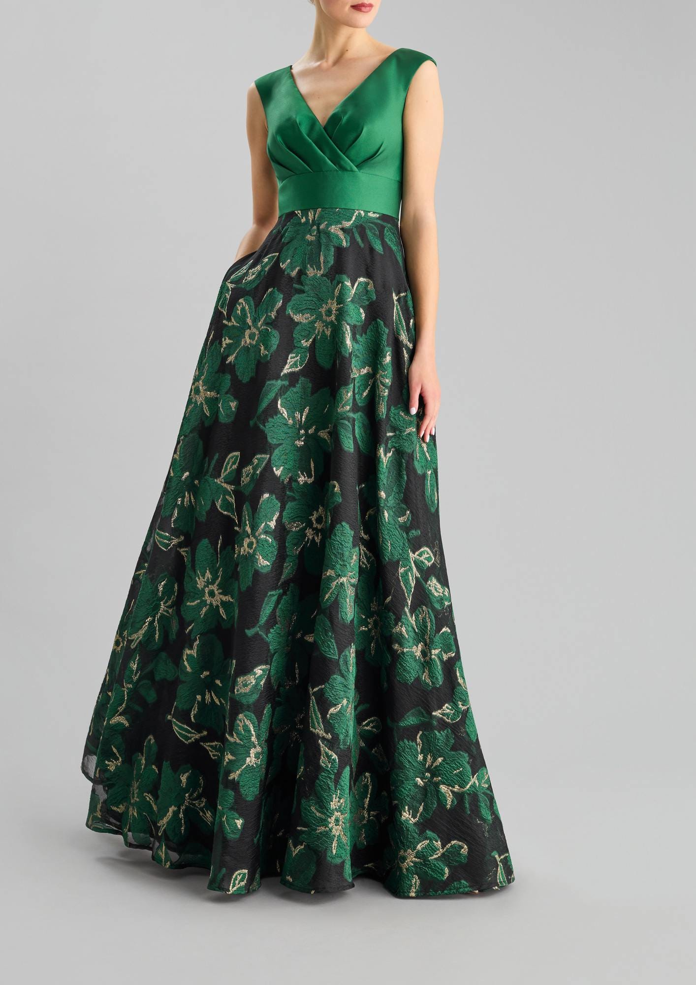 Woman wearing a green A-line wedding guest dress with V-neck, featuring floral motifs, against a grey background