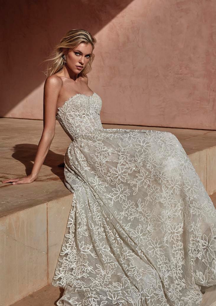 Blonde wearing a strapless A-line glittery wedding dress with plunging sweetheart neckline, sitting on steps outside. 