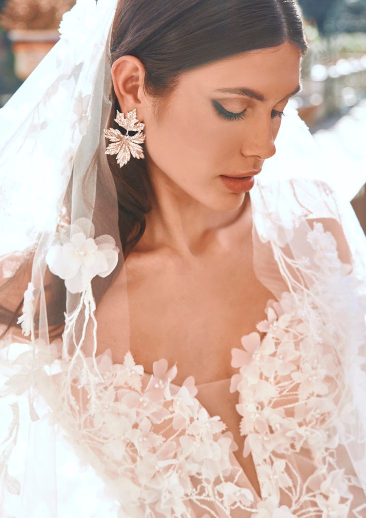 Braunhaarige Braut in schulterfreiem Brautkleid mit Brautschleier und großen Ohrringen 