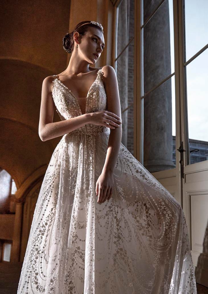Woman wearing a romantinc princess A-line wedding dress, standing gracefully in a room, gazing outside
