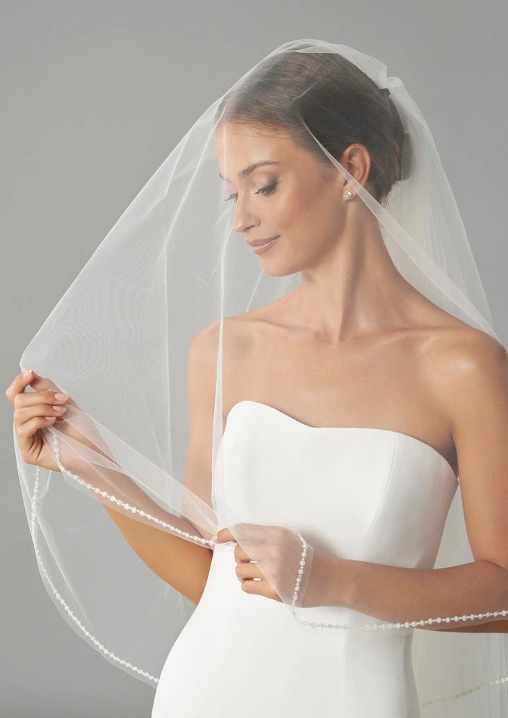 Brunette wearing a strapless bridal dress, holding and looking at a delicate wedding veil