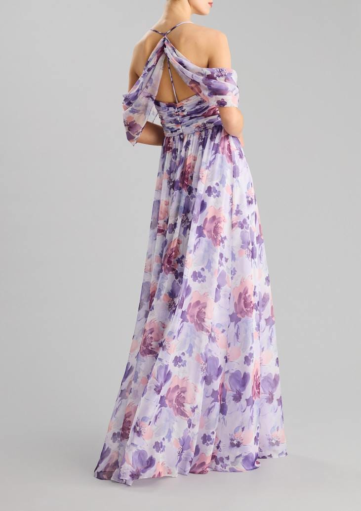 Woman wearing an A-line party gown with crossed back in chiffon, featuring floral motifs, standing against a grey background